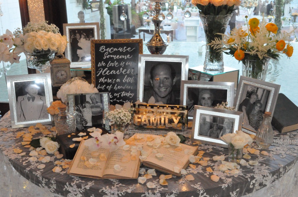 A memorial table of family photographs and white flowers at a wedding reception, honouring loved ones who are present in memory.